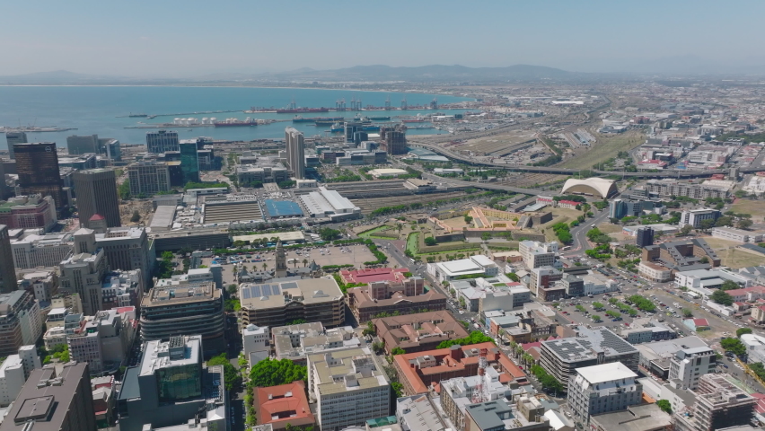 Aerial panoramic footage of city with harbour in distance. Backwards reveal of multistorey buildings. Cape Town, South Africa