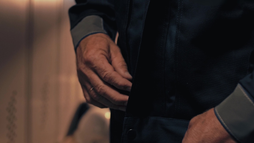 Mature production worker zips up the zipper of his protective uniform before starting his night shift. Close-up. Cinematic  Royalty-Free Stock Footage #1092498333
