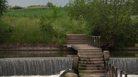 The original bridge crosses the river. Nearby is a beautiful wide waterfall. The road goes into a cornfield.