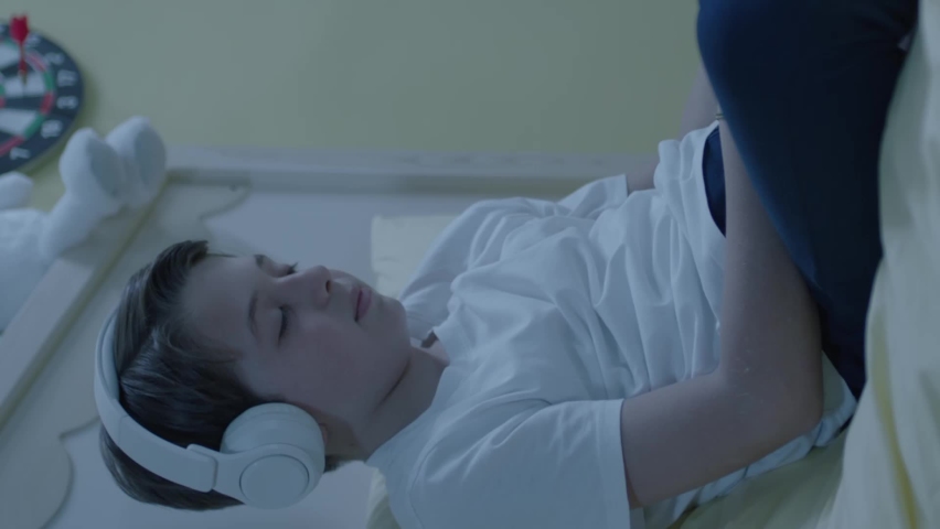 Little boy listening to music with smartphone and headphones in his bed. Child listens to audiobooks on smartphone,watches funny videos,makes video calls with friends.Portrait of boy using technology.