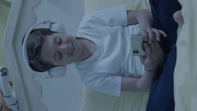 Little boy listening to music with smartphone and headphones in his bed. Child listens to audiobooks on smartphone,watches funny videos,makes video calls with friends.Portrait of boy using technology.