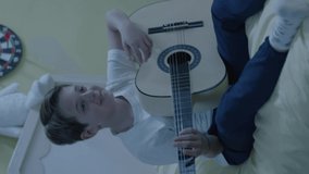 A loving boy who loves to play the guitar alone on the bed in his room. The boy who plays the guitar wants to be a musician. Concept of playing musical instrument in children.Video for the vertical.