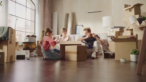 Happy Homeowners Moving In: Lovely Couple in New Cozy Apartment Living Room, Unpacking Cardboard Boxes, Little Daughter Joins them. Young Family Having Fun. Stylish Cinematic Following Handheld Shot