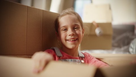 Portrait of Little Girl Plays Hide and Seek Jumping out of Cardboard Box. Pretty Cheerful Child Having Incredible Fun in the Sunny Apartment Living Room. Happy, Laughing, Cute Kid Enjoying Childhood