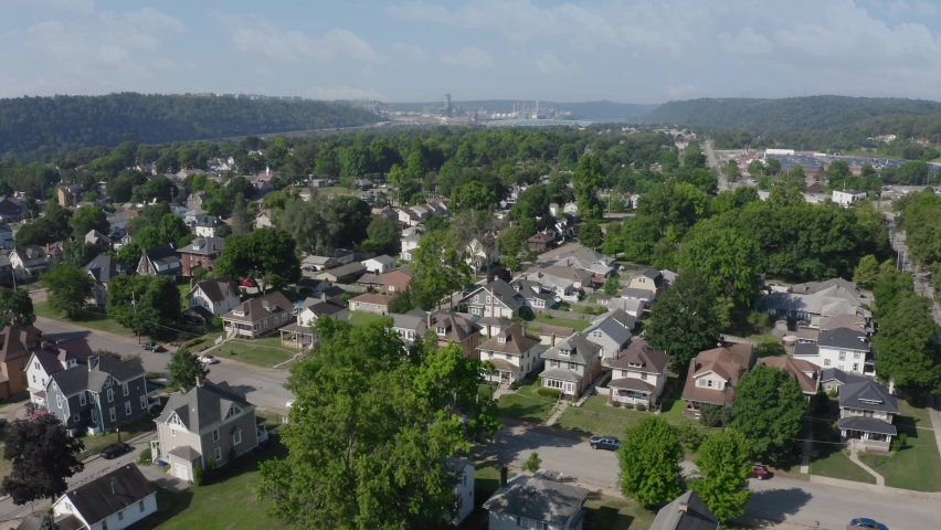 A slow forward summer aerial establishing shot of a small Pennsylvanian town. The Beaver County Shell cracker factory on the Ohio River in the distance.	