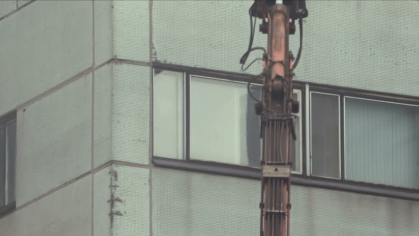 Demolition Machine. A large tracked excavator machine fitted with concrete crunching demolition tool, ripping apart old building.