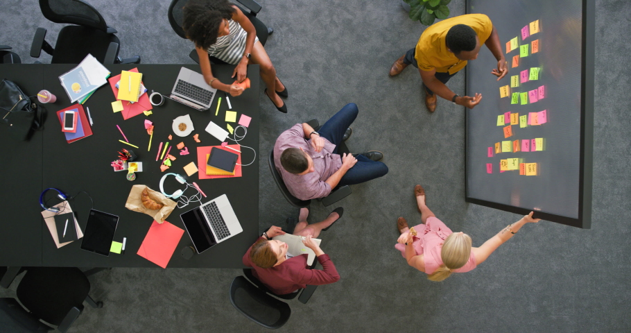 Teamwork of successful businesspeople meeting together from above, cheering with high five gesture after completing visual aid brainstorm. Diverse group of marketing agents planning workshop strategy