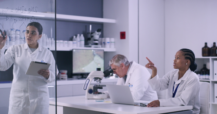 Biologists or chemists brainstorming cure for covid. Doctors discussing a chemical formula for a clinical trial. Diverse group of scientists analyze information on transparent board in chemistry lab. Royalty-Free Stock Footage #1092518067