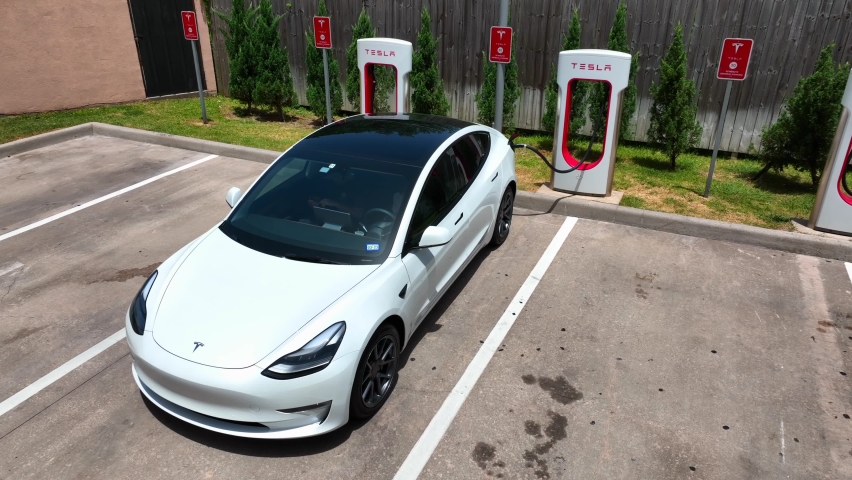 Houston , Texas , United States - 06 13 2022: Close up of Tesla Model 3 charging battery at a Tesla supercharger station. Aerial view of white vehicle. 