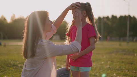 Mother applies decongestant cream onto swollen eyelid of little daughter in park. Insect bite allergic reaction. First air for hurt child
