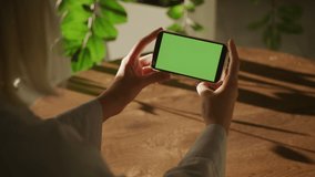 Handheld over the shoulder close up shot of a woman holding smart phone with green screen chroma key