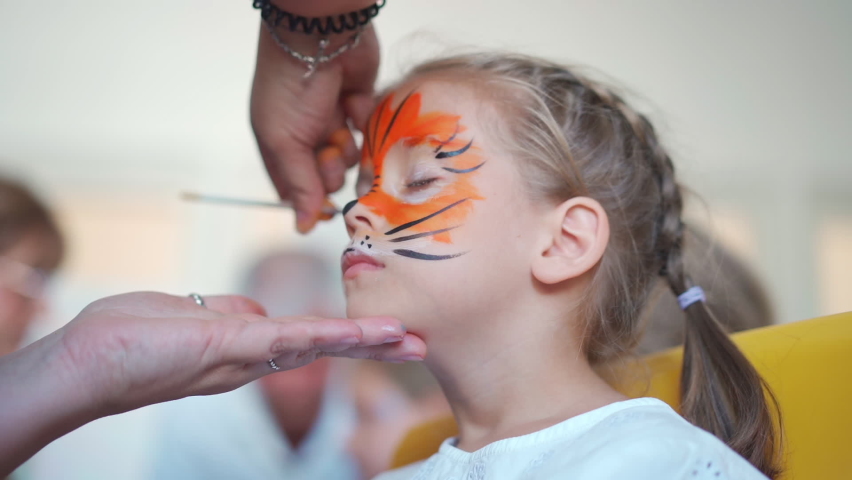 Children face painting. Artist painting with brash and special body paint tiger mask on face of little girl on carnival party for children. Body art painting for childrens. Royalty-Free Stock Footage #1092529167