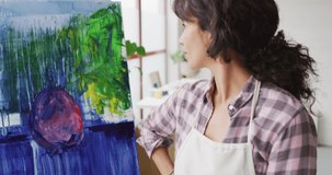Video of happy biracial female artist posing with painting in studio. Art, crafts, creativity and creation process concept.