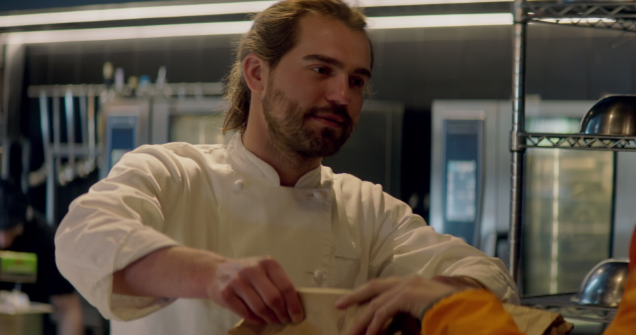 TRACKING CU Portrait of food delivery courier in bicycle helmet leaving a restaurant after picking up order for delivery. Shot with 2x anamorphic lens