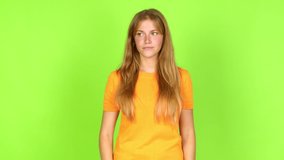 Young pretty blonde woman on green screen chroma key covering eyes by hands and looking through the fingers over isolated background