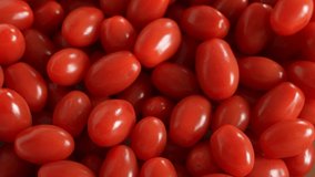 Closeup top view 4k stock video footage of several red small oblong cherry tomatoes falling down on pile of many blurry tomato vegetables background