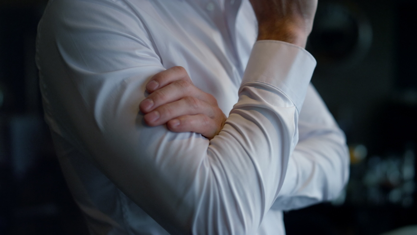 Unknown elegant businessman standing dark restaurant interior. Closeup folded man hands. Unrecognizable entrepreneur thinking making decision in lounge cafe. Body language concept. Confidence concept.