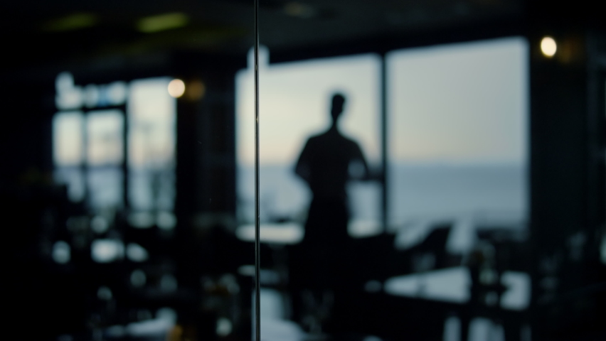 Focused man silhouette looking beautiful view in dark panoramic bar. Handsome boss waiting business meeting in restaurant. Charming businessman enjoying time in lounge cafe. Modern lifestyle concept. Royalty-Free Stock Footage #1092556703