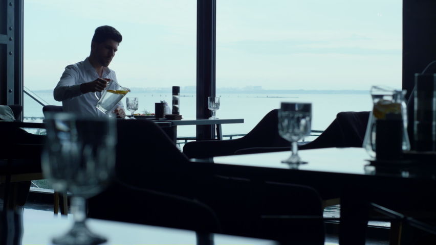 Handsome guy resting sea view hotel lounge cafe alone. Attractive entrepreneur silhouette waiting business meeting in stylish restaurant. Elegant man pouring refreshing drink glass at luxury lunch.
