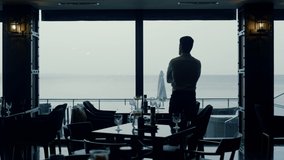 Elegant businessman silhouette enjoying ocean view in panoramic cafe. Pensive man spending dinner time thinking in dark interior back view. Stylish guy looking restaurant windows. Loneliness concept. - Powered by Shutterstock - Get 15% off with code: PIKWIZARD15
