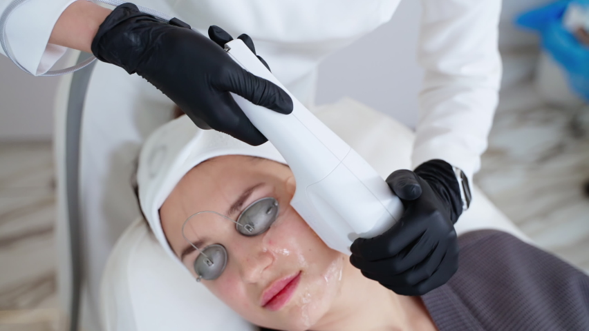 aesthetic procedure in modern cosmetology clinic, expert beautician is using phototherapy apparatus for middle-aged woman patient, rejuvenate and anti-wrinkle effect Royalty-Free Stock Footage #1092564139
