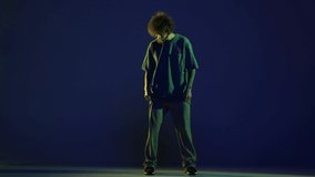 Emotions. Stylish young man, hip-hop dancer wearing sport casual style outfit dancing isolated over dark blue background in neon light. Modern dance art, fashion, youth, ad, style concept. 4K, video