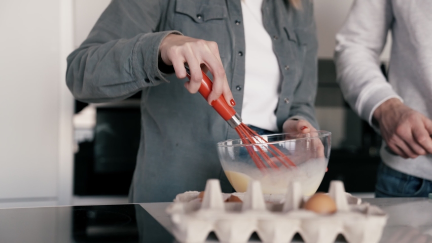 Smiling woman mixes omelet mixture while her boyfriend cuts tomatoes