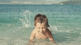 Slow motion video of a baby boy smiling and swimming in the sea. Child on summer vacation happy splashing in the ocean on the beach.
