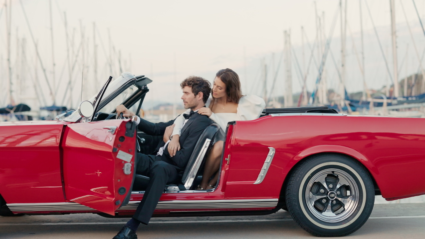 Young Couple In Red Car. Girl Sitting Behind Man. Pretty Brunette In White Dress Hugs Man.