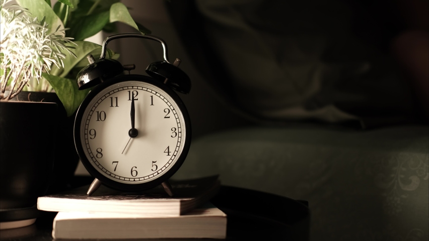 The alarm clock is on the night table in the bed room with plant pot on a book. and the man who slept in bed all night until morning. the clock shows the time from night until morning. timelapse. 4k Royalty-Free Stock Footage #1092588023