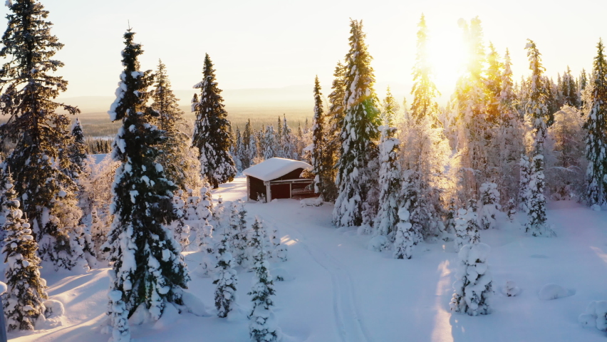 Aerial view across glowing morning sunrise shining through snow covered woodland trees and idyllic rural cabin Royalty-Free Stock Footage #1092589221