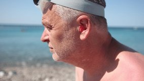 Mature man putting silicone ear plugs, surfers earplugs, swim plugs