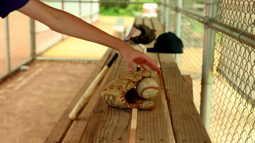 Baseball player picks up ball and glove off dugout bench
