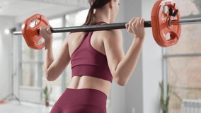 view from the back. a beautiful and slender young woman does exercises with dumbbells in the gym. video and online lessons for sports. clothes and shoes for gymnastics. professional fitness trainer.