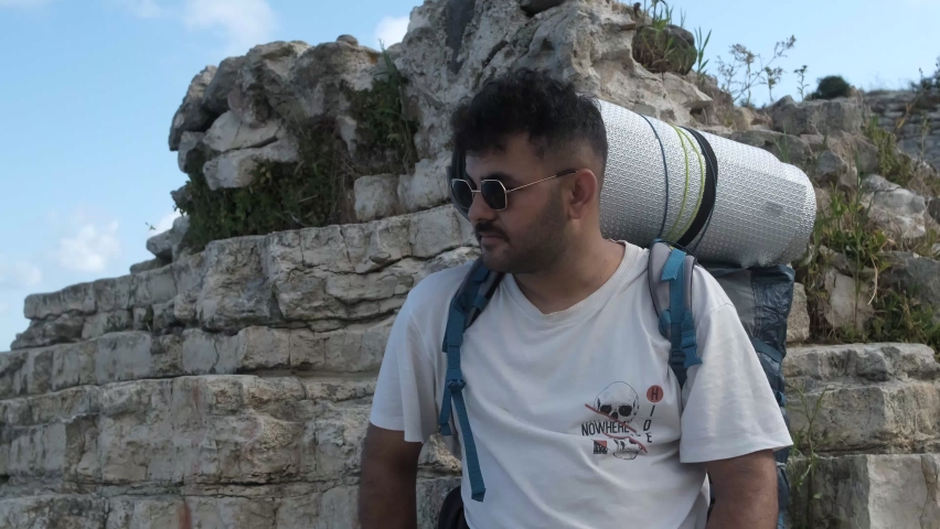 Backpacker camper boy, young male resting with camping gear in backpack, view of camper wearing glasses viewing scenery, looking araound with camping gear