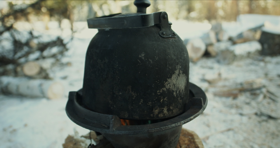 An old tourist kettle with black soot on the walls, heated on a burner, in a winter forest