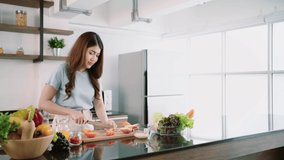 A happy young Asian woman preparing a healthy salad with vegetables on a cutting board on the home kitchen counter. Food cooking for couple husband and wife in a good relationship. Real time 4k video.