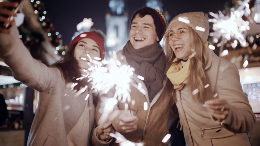 Happy young multiracial friends asian girl use a smartphone communicating, podcast video chat Europe night street. Woman looking at phone selfy with falling sparkling glowing sparklers fireworks light Royalty-Free Stock Footage #1092610273