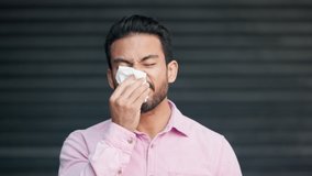 Sick, allergic and sneezing young man. Irritated Male blowing nose in tissue, having a reaction to particles in the air. Isolated guy over background sneezing into disposable paper towel. - Powered by Shutterstock - Get 15% off with code: PIKWIZARD15