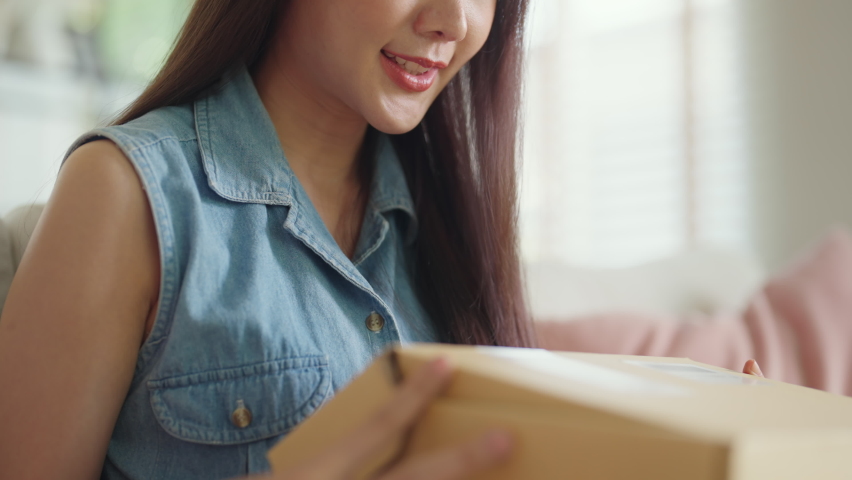 Young Gen Z influencer girl open gift postal mail box sit at home sofa couch. Asia people enjoy wow unbox carton parcel order online buy from small retail store SME shop supply chain omni channel. | Shutterstock HD Video #1092618723