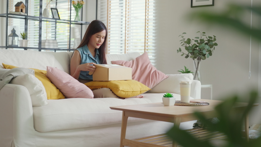 Young Gen Z influencer girl open gift postal mail box sit at home sofa couch. Asia people enjoy wow unbox carton parcel order online buy from small retail store SME shop supply chain omni channel. | Shutterstock HD Video #1092618725