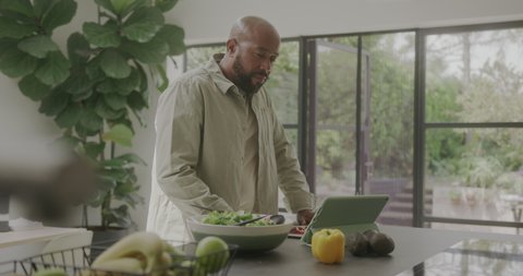 Стоковое видео: Mature Male in Kitchen using Digital tablet Preparing Healthy Food
