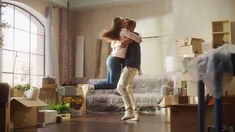Family New Home Moving in: Happy Girlfriend Returns Home and Finds Her Happy Man Doing Unpacking, They Hug and Dance. Happy Couple in their Cozy Sunny Apartment. Mortgage Loan, Home Renovations