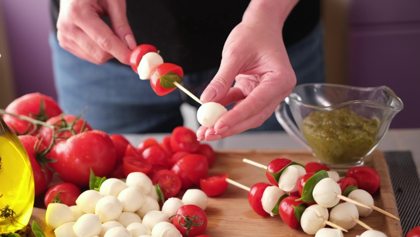 Making caprese canapes sticking cherry tomatoes and mozzarella cheese balls on a skewer | Shutterstock HD Video #1092630513