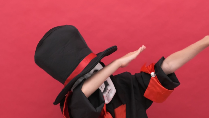 Halloween kids Happy dancing boy in Halloween skeleton costume Trick or treating. red background A man in a skeleton costume and a hat is dancing a crazy dance