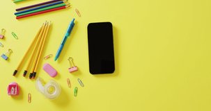 Video of composition of diverse office tools and smartphone with copy space on yellow background. School equipment, tools, learning and education with technology concept.