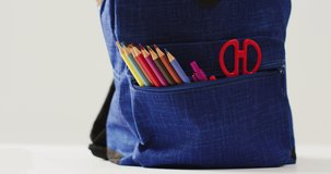 Video of backpack with crayons, rulers and scissors over beige background. School equipment, tools, learning and education concept.