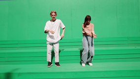 Young couple dancing hip hop on green background wall. Modern dance choreography. Professional dancers man and woman duet showing dance movings. Musical video.