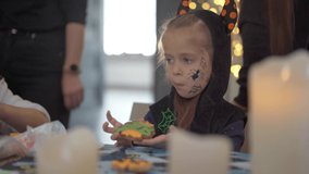 Little girl eat icing just making handmade Halloween cookies sitting on the table dressed Halloween carnival costume with horns . Halloween party in big family. High quality 4k footage - Powered by Shutterstock - Get 15% off with code: PIKWIZARD15