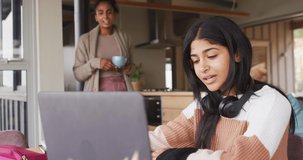 Video of happy biracial woman in headphones learning with laptop at home. Education and learning from home with technology.